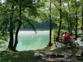 Spokojny poranek na polu kempingowym nad jeziorem. Mgła unosi się nad wodą, a przy stole siedzi kilku mężczyzn.