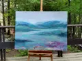 Un paysage abstrait aux teintes bleues et vertes, évoquant des montagnes brumeuses et un lac. Le fond de tableau peinture est posé sur un chevalet, en extérieur, entouré de verdure.