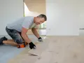 Mężczyzna w rękawiczkach układa deski drewnianej podłogi.