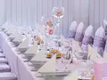 Vacker dukning med rosa rosor i glasvaser, vita servetter och silverfärgade skålar på en rosa bordsduk.