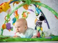 Niemowlę leży na kolorowej macie edukacyjnej, bawiąc się wiszącymi zabawkami: żyrafą, papugą i zebrą.