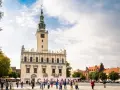 Rynek w Chełmnie z ratuszem i tablicą z napisem "Chełmno". Ludzie spacerują, podziwiając atrakcje miasta.