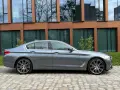 Szary sedan BMW G30 na tle nowoczesnego budynku.