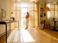 Una donna guarda fuori dalla finestra, mentre il sole crea ombre sul parquet che scricchiola. Un angolo studio e un tavolo da pranzo completano l'ambiente.