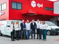 Zespół DPD pozuje przed budynkiem z logo firmy i elektrycznym dpd bus.