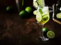 Orzeźwiający Hugo Spritz z limonką i miętą, otoczony świeżymi limonkami na drewnianym blacie.