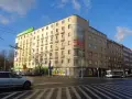 Charakterystyczny budynek z balkonami i zaokrąglonym narożnikiem, przykład modernizmu w architekturze, na tle błękitnego nieba.