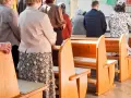 Ludzie stoją w kościele, czekając na dyspensę. Widać ławki i fragmenty ubiorów wiernych.