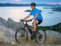 Man riding a mountain bike on a rocky trail overlooking a serene bay at dusk.