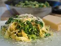 Makaron tagliatelle ze szpinakiem i startym parmezanem, obok kawałek sera.