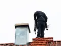 Kominiarz na dachu z narzędziami. Zastanawiasz się, ile kosztuje czyszczenie komina? To ważna usługa dla bezpieczeństwa.
