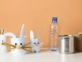 Zające z rolek po papierze i puszek to świetne przykłady recyklingu w życiu codziennym. W tle pusta butelka i rolka po ręczniku papierowym.