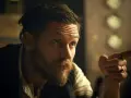 Mężczyzna z charakterystyczną fryzurą w stylu Peaky Blinders, z zarostem i pierścieniami na palcach, wskazuje palcem.