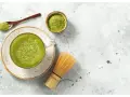 Zielona, spieniona matcha w filiżance, obok bambusowa miotełka i łyżeczka z proszkiem. To właśnie co to matcha – napój pełen energii.