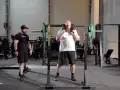 Man med skägg förbereder sig för knäböj med en safety squat bar. En tränare står bredvid.