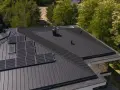 Nowoczesny dach z ciemnoszarą blachą na rabek, panele fotowoltaiczne i okno dachowe.