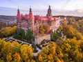 Zamek Książ otoczony jesiennym lasem, z widoczną palmiarnią w oddali.