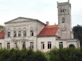 Pałac Rekowo, z wieżą i czerwoną dachówką, otoczony zielenią.