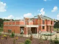 Rozbudowa domu w toku. Czerwone ściany z pustaków, betonowe stropy i drewniana konstrukcja dachu tworzą zarys przyszłego domu.