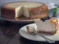 Sernik pieczony z polewą jagodową, a w tle cały sernik. Idealny wybór: sernik pieczony czy sernik na zimno?