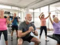 Groupe de seniors pratiquant le renforcement musculaire en salle de sport, avec haltères et élastiques.