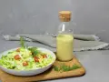 Frischer Salat mit Tomaten und Mais, daneben eine Flasche mit cremigem Jogurt Dressing und Dill.