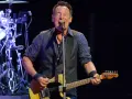 Bruce Springsteen singt und spielt seine ikonische Bruce Springsteen Gitarre auf der Bühne, während die Band im Hintergrund spielt.