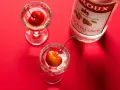 Zwei Gläser mit Kirschen und eine Flasche Kirschwasser auf rotem Hintergrund. Was ist Cherry? Ein süßer Genuss.