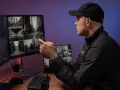 Vigilante revisa su móvil mientras monitorea cámaras de seguridad. La **nocturnidad** se refleja en las imágenes de las calles.