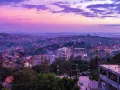 Fioletowe niebo nad krajem z kampalą, z widokiem na wzgórza pokryte zabudowaniami i zielenią.
