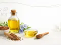 Olej lniany w butelce i miseczkach, nasiona lnu na łyżkach i w misce, niebieskie kwiaty lnu. Czy olej lniany jest zdrowy? Tak, to bogactwo kwasów omega-3.