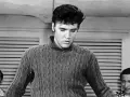 Elvis Presley in einem Strickpullover, vielleicht bei der Aufnahme seines letzten Liedes. Im Hintergrund zwei Männer.