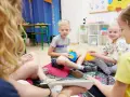 Chłopiec, około 10 lat, siedzi na podłodze z niebieską zabawką. Wokół niego inne dzieci.