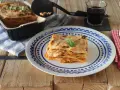 Una porción de lasaña de atún, dorada y gratinada, servida en un plato con diseño azul.