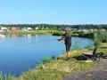 Mężczyzna łowi ryby na spokojnym jeziorze, ciesząc się darmowe łowiska. W tle widać domy i las.