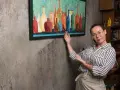 Une femme explique comment vernir un tableau, montrant une œuvre colorée de bouteilles.