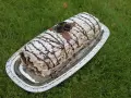 En läcker budapestrulle recept på ett silverfat, dekorerad med chokladrosor och pudersocker, på en grön gräsmatta.