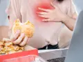 Kobieta z bólem w klatce piersiowej trzyma hamburgera. Zastanawia się, co pić na zgagę po zjedzeniu pizzy i fast foodów.
