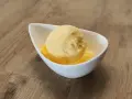 Ein Löffel cremiges Mandarinen Eis in einer weißen Schale auf Holzhintergrund.