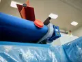 Maszyna do produkcji folii, z niebieskim wałkiem i pomarańczową nakrętką, przygotowuje materiał cerplast do dalszej obróbki.