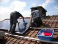 Dwóch mężczyzn montuje panele fotowoltaiczne na dachu. Czy panele fotowoltaiczne trzeba zgłaszać? Instalacja trwa.