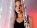 A young woman peeks through crinkled plastic sheet materials, her face illuminated by soft, colorful light.
