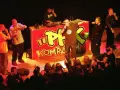 Raperzy na scenie przed czerwonym banerem z napisem "PFK Kompakt", publiczność w pierwszym rzędzie.