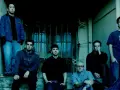 Sześciu członków zespołu Linkin Park, w tym Chester Bennington, pozuje na schodach.
