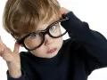 Chłopiec z niebieskimi oczami poprawia okulary, zastanawiając się nad nadwzrocznością u dzieci kiedy okulary są potrzebne.
