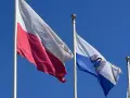 Flaga Torunia i biało-czerwona flaga Polski powiewają na tle błękitnego nieba.