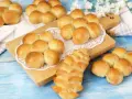 Morbidi panini al latte dorati, alcuni disposti a grappolo su un tagliere, altri su un panno bianco.
