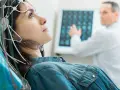 Frau mit EEG-Kappe für eeg medizinische Untersuchung, Arzt deutet auf Bildschirm mit Gehirnscans.
