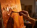 Main d'artiste appliquant la peinture à l'huile avec un pinceau, créant une texture riche sur la toile. La technique de peinture à l'huile est mise en valeur.