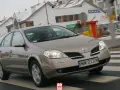 Brązowy Nissan Primera przejeżdża przez pasy na tle zaśnieżonych domów.